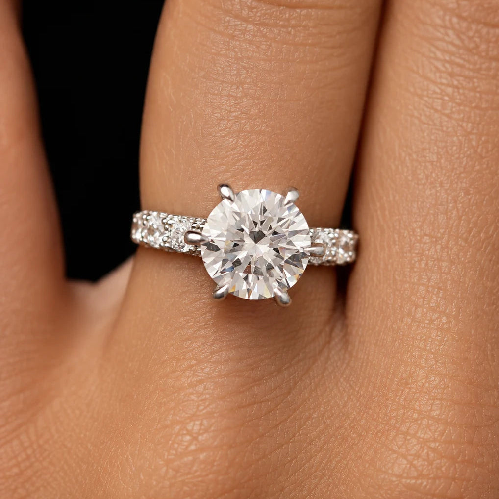Round cut solitaire engagement ring with sparkling pave band worn on model finger