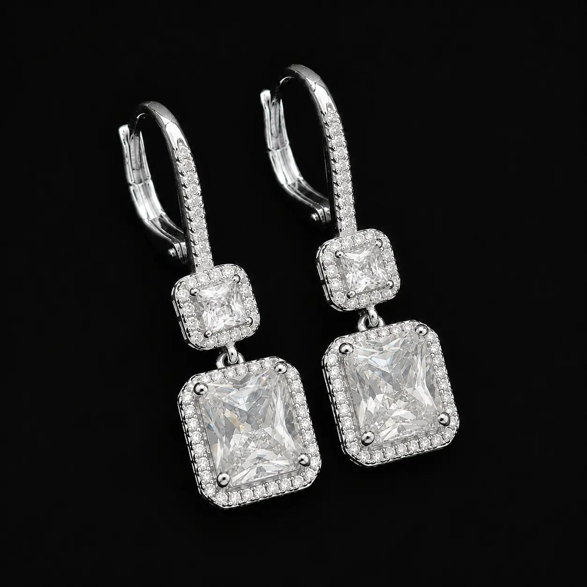 left side view of sparkling two-tiered square halo dangle earrings on black background.