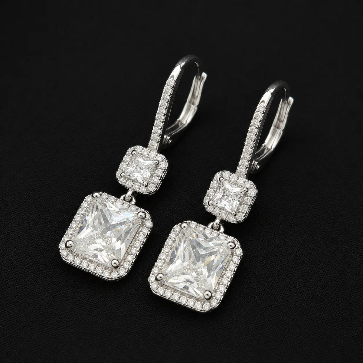 Angled side view of sparkling two-tiered square halo dangle earrings on black background.